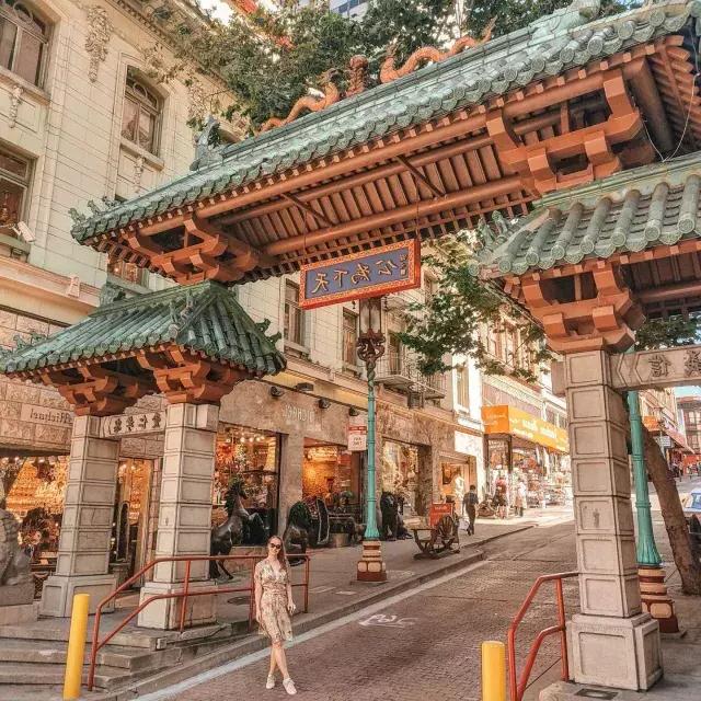 Una donna posa davanti a un cancello decorato che segna l'ingresso della Chinatown di San Francisco.